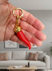 Red chili pepper-shaped keychain with gold accents held in a hand against a white background