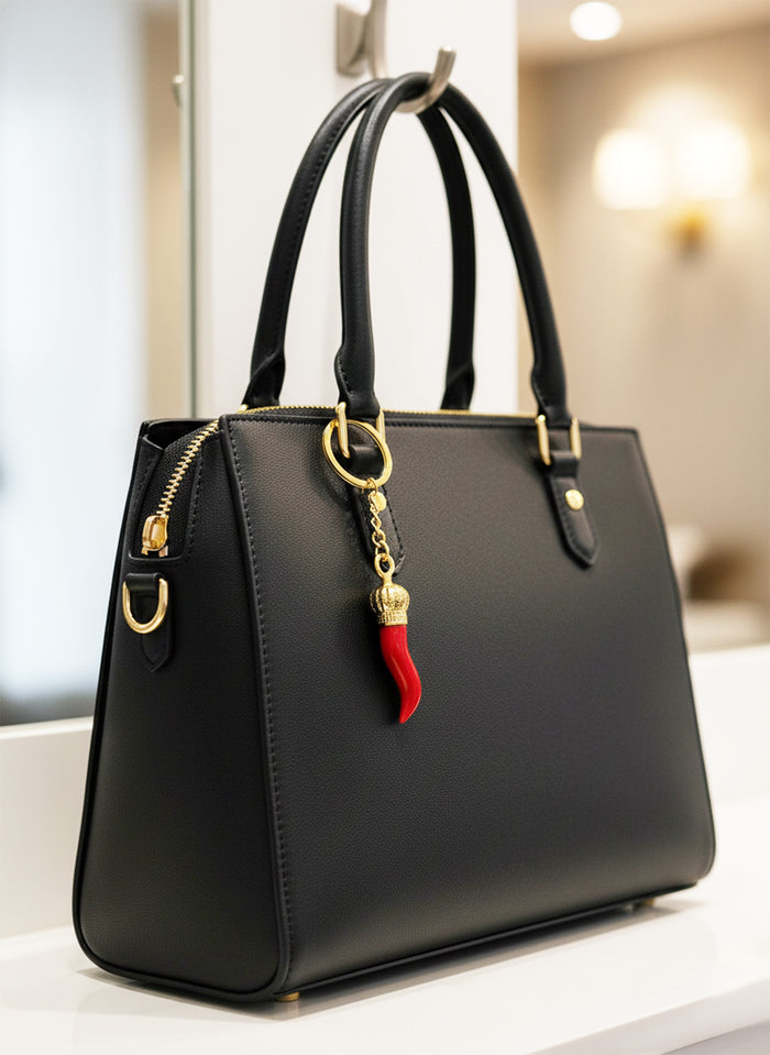 Black handbag with a red and gold charm on a blurred indoor background