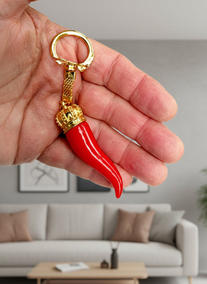 Red chili pepper-shaped keychain with gold accents held in a hand against a white background