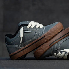 A pair of low-top platform sneakers with a dark gray suede and leather upper, white laces, and a thick brown platform sole, displayed on a dark textured surface.